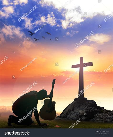 Silhouette Man Kneeling With Hand Holding Guitar Over The Cross On A