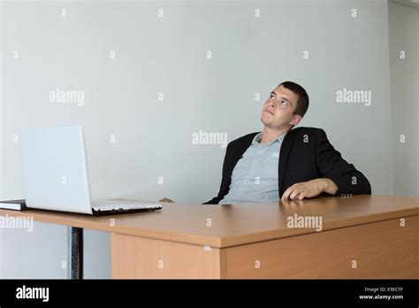 Young Businessman Sitting At His Table Area Looking Up While Thinking A