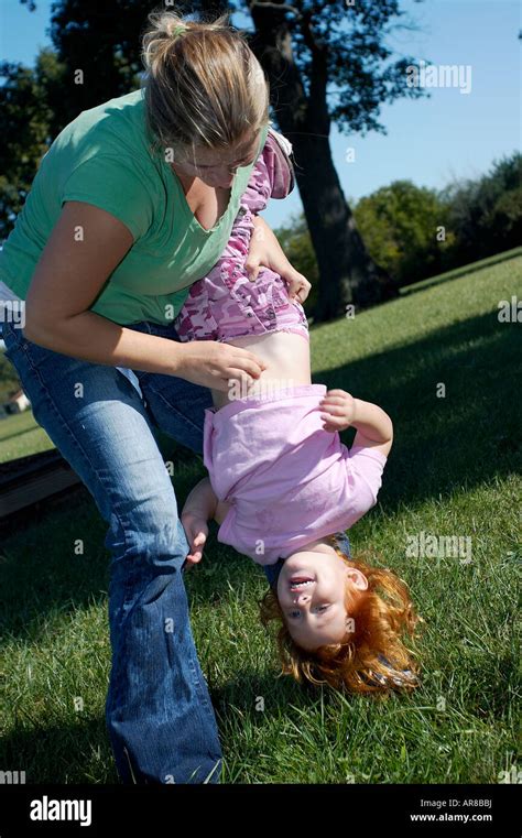 A Young Mother Holding Her Daughter Upside Down And Tickling Her Stock