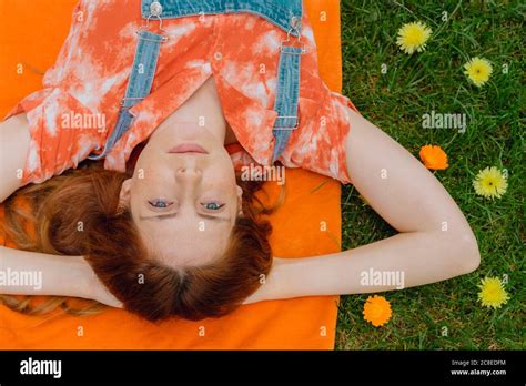 Relaxed Young Woman Lying With Hands Behind Head On Picnic Blanket By Flowers At Back Yard Stock