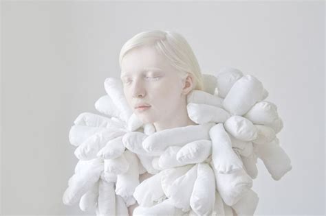 A Woman With White Hair Is Wearing A Large Pile Of Pillows On Her Head And Neck