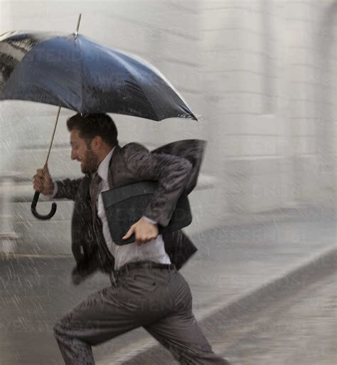 Businessman With Umbrella Running In Rain Stock Photo