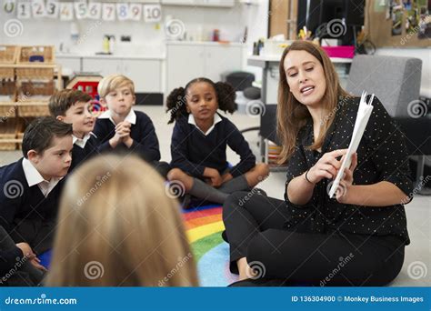 Young Female Primary School Teacher Reading A Book To Children Sitting