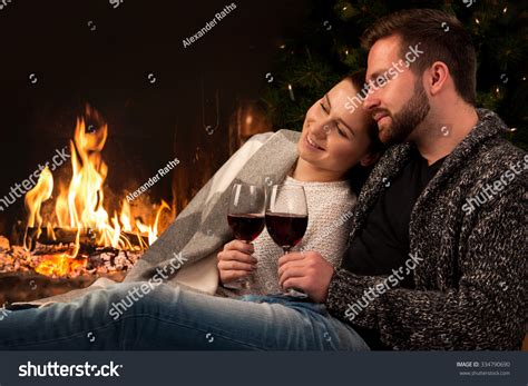 Couple Relaxing With Glass Of Wine At Romantic Fireplace
