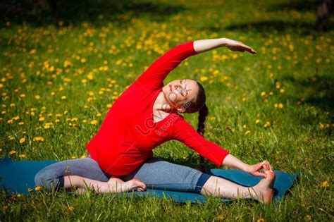 pregnant woman doing parivrtta janu sirsasana revolved head to knee pose outdoors on grass lawn