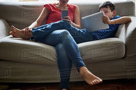Mother And Son Relaxing On Sofa Using Digital Tablet And Smartphone