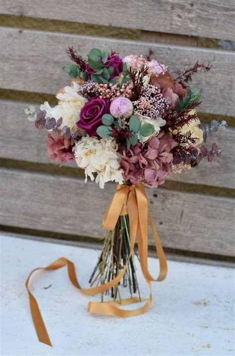 A Bridal Bouquet With Purple Flowers And Greenery Tied Around It On A Bench