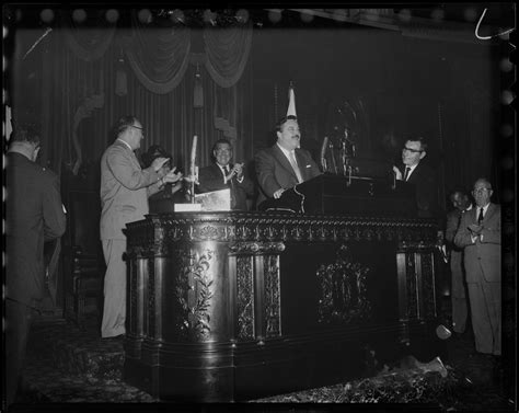 Man and house for sale. Filmstage-television comedian Jackie Gleason stands with other men at a speaker's podium as he ...