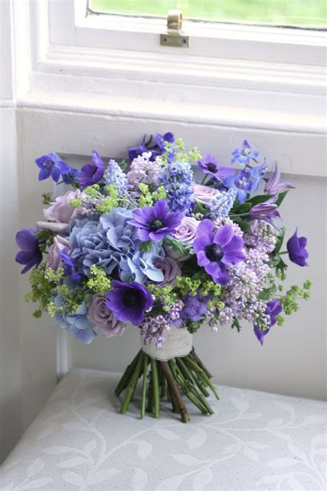 A Bouquet Of Blue And Purple Flowers Sits On A Bench In Front Of A Window