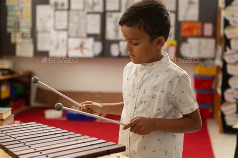 Side View Of Cute Mixed Race Schoolboy Playing Xylophone In A Classroom