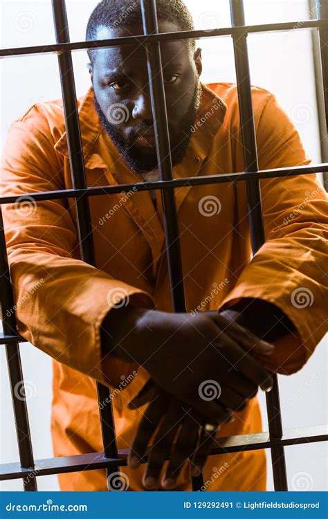 African American Prisoner Leaning On Prison Bars And Looking Stock