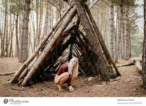 Barefoot Woman Squatting Beside Primitive Shelter In Woods A Royalty Free Stock Photo From