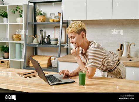 Contemporary Businesswoman With Laptop Bending Over Kitchen Table
