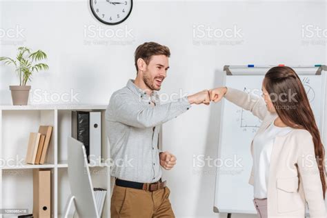 Happy Young Businessman Giving Fist Bump To Smiling Female Coworker In