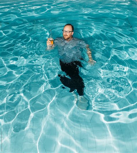 Young Fully Clothed Male Drinks A Beer While Swimming In A Pool During A Party At Night By