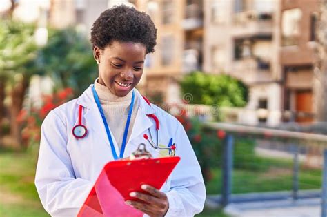 African American Woman Wearing Doctor Uniform Writing On Clipboard At