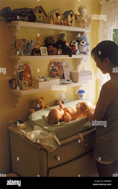 Mother Changing Babies Diaper At Home Under Shelves Of Baby Toys Stock