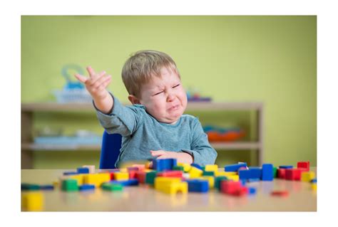 Boy at table with blocks holding one hand up and crying