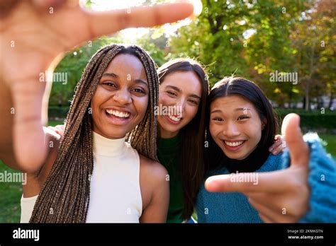 Three Interracial Friends Taking Selfie Making Hand Frame Gesture At Natural Park Looking At