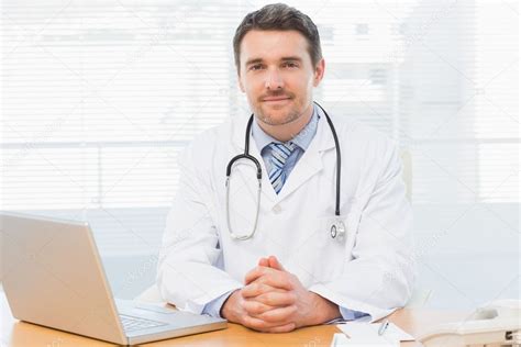 Male Doctor With Laptop At Desk In Medical Office Stock Photo By