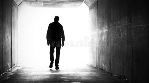 A Silhouette Of A Man Walking Out Of A Dark Tunnel Towards The Light