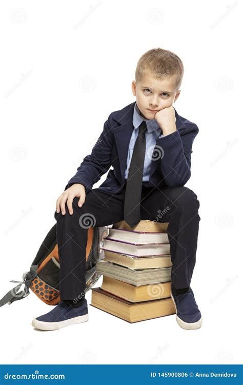 Cute Sad Schoolboy Sitting On A Stack Of Books Isolated On A White