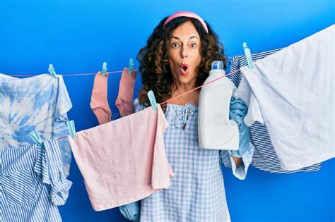 Middle Age Hispanic Woman Doing Laundry Holding Detergent Bottle Scared