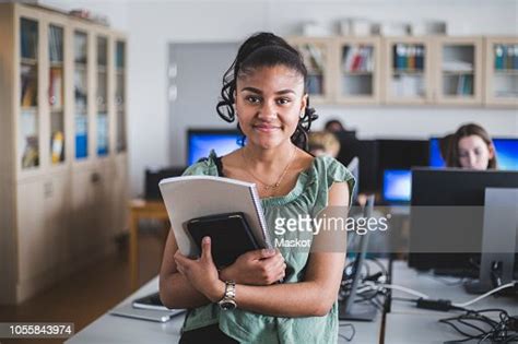 Portrait Of Smiling Teenage Girl Standing With Book In Computer Lab At