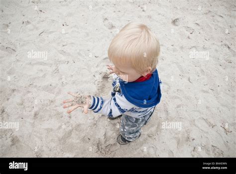 Child Looking At Sand In His Hand In A Childrens Sandpit Stock Photo