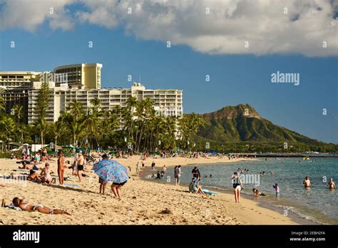 People Relaxing And Sunbathing On The Waikiki Beach Surrounded By Resorts With Volcanic