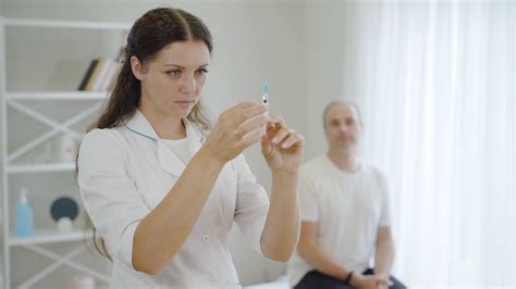 Young Beautiful Woman With Syringe Standing In Hospital Ward With Blurred Stressed Man At The