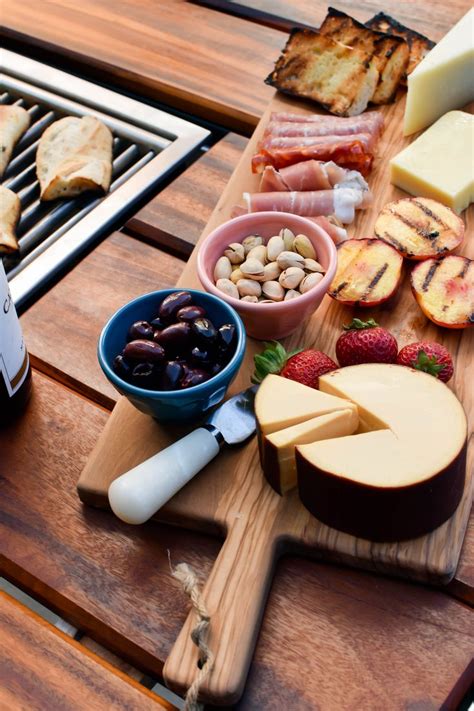 A Wooden Cutting Board Topped With Cheese Fruit And Crackers On Top Of