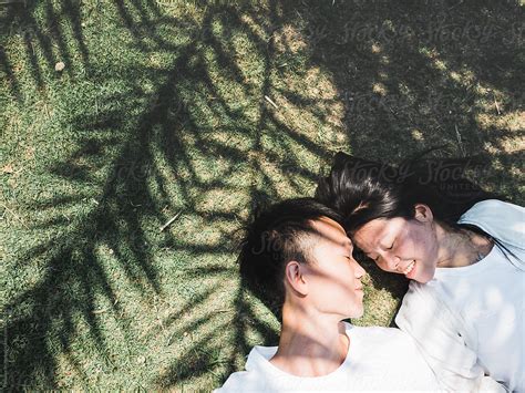Chinese Young Couple Lying On Ground With Palm Tree Shadow By Stocksy