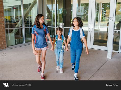 Three Girls Holding Hands Walking Outside Of School Together Stock