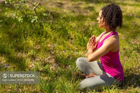 relaxing biracial woman practicing yoga sitting with crossed legs and meditating in countryside