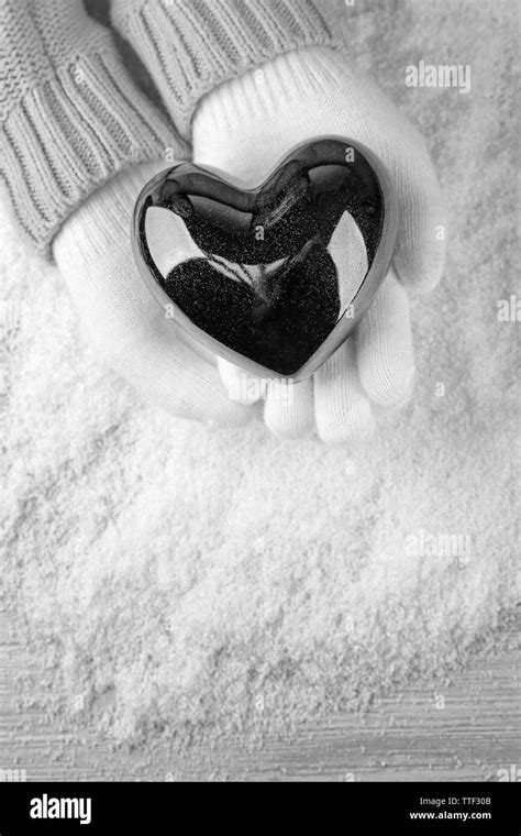 Hands In Warm White Gloves Holding Black Heart On Snowy Background