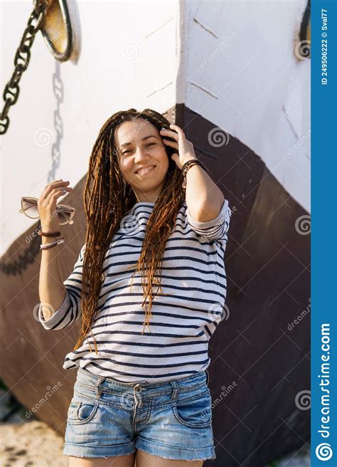 A Girl With A Dreadlocked Hairstyle Poses On The Beach Near A Ship In