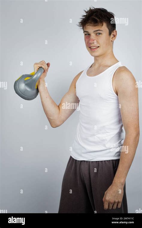 A 17 Year Old Teenage Boy Wearing A White Tank Top Lifting A Kettlebell