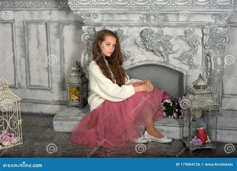 A Beautiful Pensive Girl In A White Sweater And Pink Skirt By The