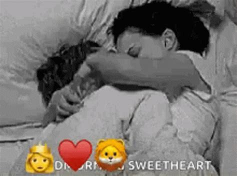 Two People Hugging Each Other In Bed With Emoticions On The Wall Behind