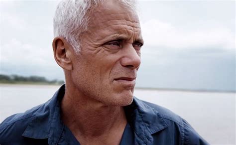 An Older Man With White Hair Standing In Front Of The Water Looking Off Into The Distance