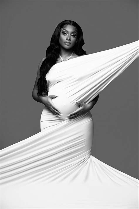 A Pregnant Woman In A White Gown Posing For A Black And White Photo With Her Hands On Her Hips