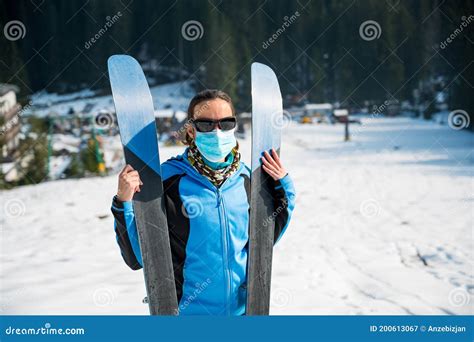 Female Skier Posing With A Pait Of Skis Wearing Protective Face Mask