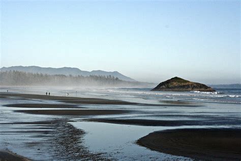 People Are Walking On The Beach In Front Of Some Hills And Water With Low Tide