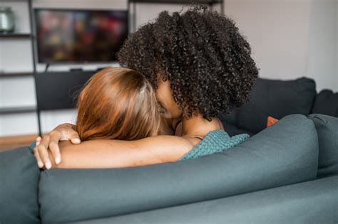 Lesbian Multiracial Couple Watching Tv Tenderly Hugging In Living Room At Home Sweet Couple
