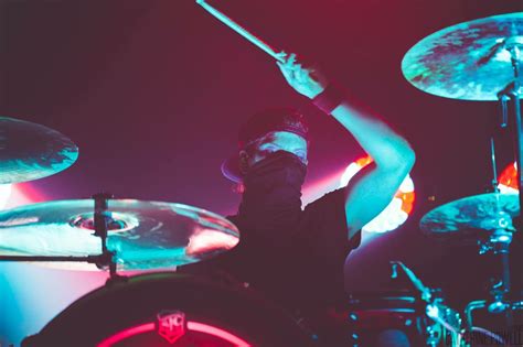 A Man Playing Drums In Front Of Some Red And Blue Lights With His Hands Up