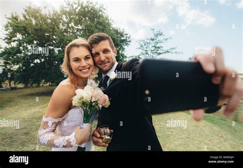 Beautiful Bride And Groom Taking A Selfie With Mobile Phone Outdoors