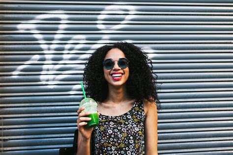 Portrait Of A Young Latin Afro Woman Drinking A Green Smoothie Standing On The Street By