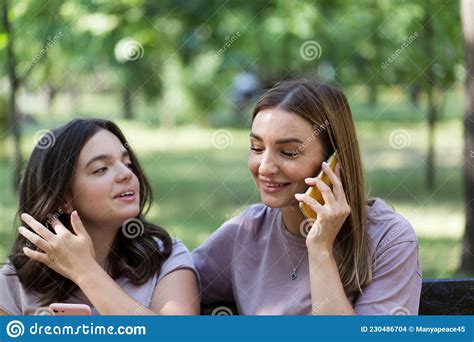 Mom And Teenage Daughter Use A Smartphone For A Walk In A Summer Park