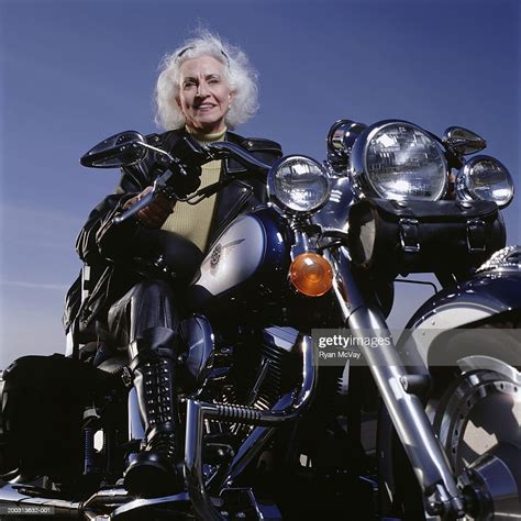 Senior Woman Wearing Leathers Sitting On Motorcycle Posing In Studio